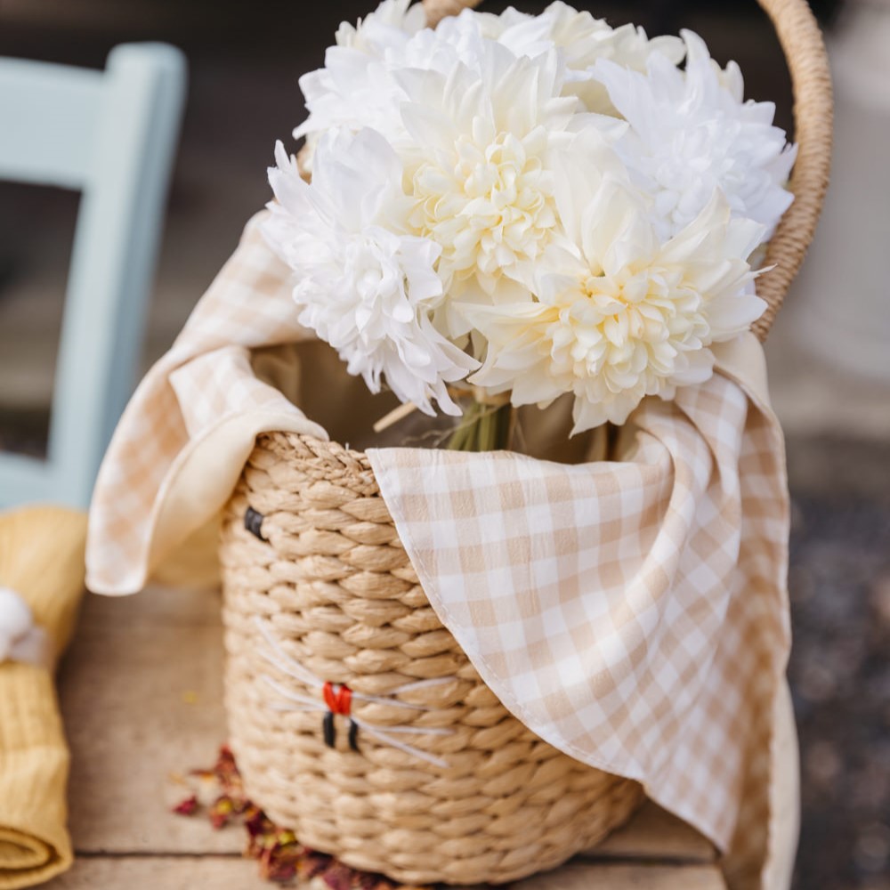 Cesta de palha com flores brancas e pano xadrez bege