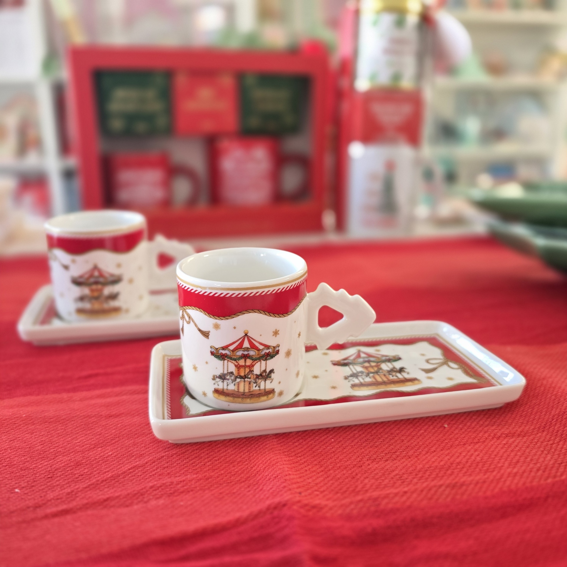 Conjunto de chávenas e bases decoradas com carrossel sobre toalha vermelha