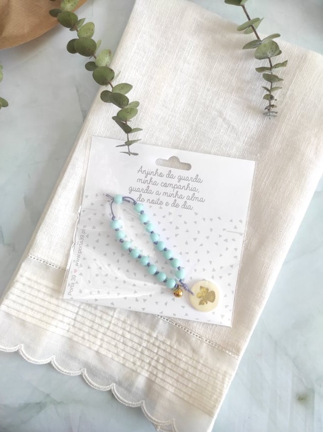 Pulseira colorida para criança com pingente numa embalagem branca sobre pano bege.