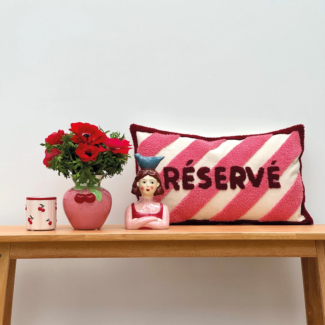 Almofada, vaso com flores, figura decorativa e recipiente em cima de mesa de madeira