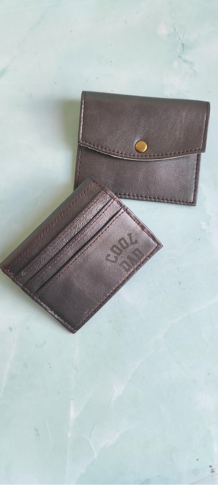 Carteira e porta-cartões castanhos em pele com inscrição COOL DUO sobre fundo verde-claro