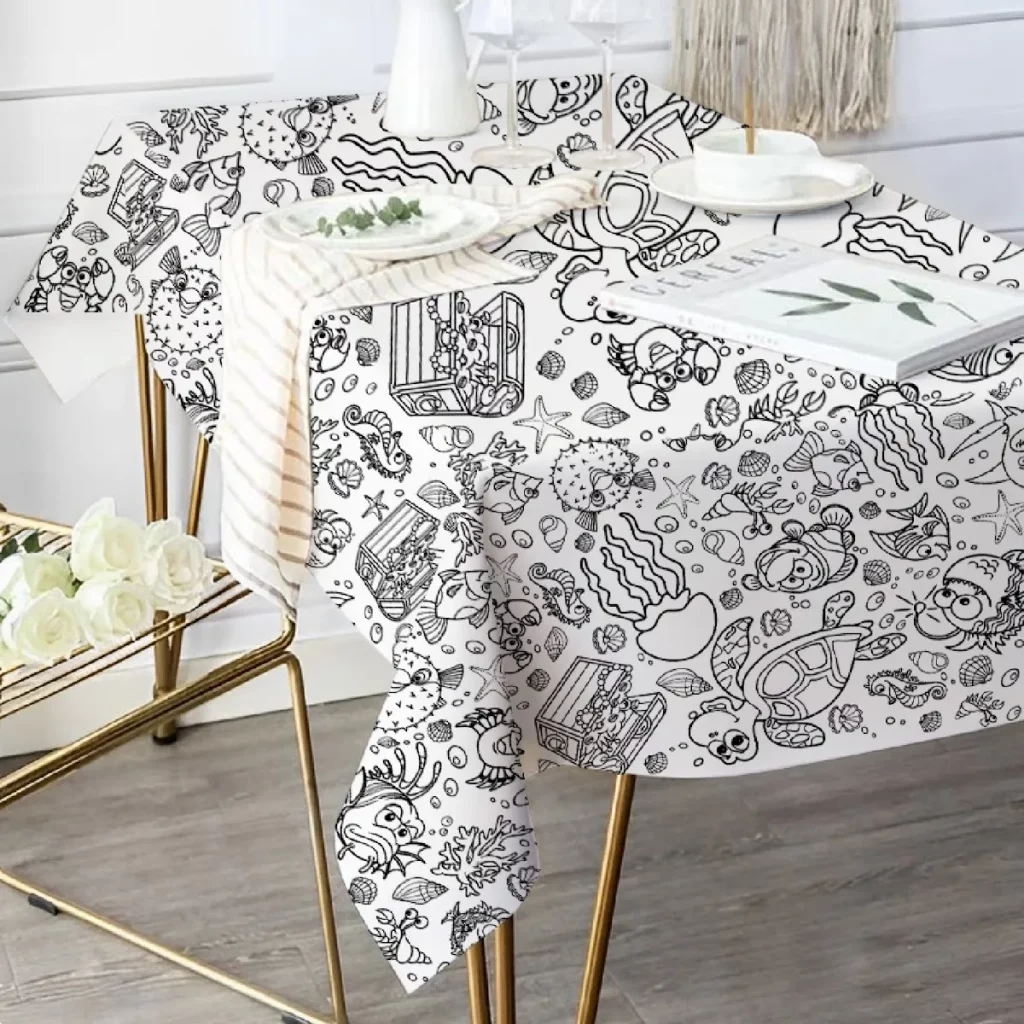 Toalha de mesa com desenhos humorísticos a preto de animais marinhos, numa mesa com pernas douradas.