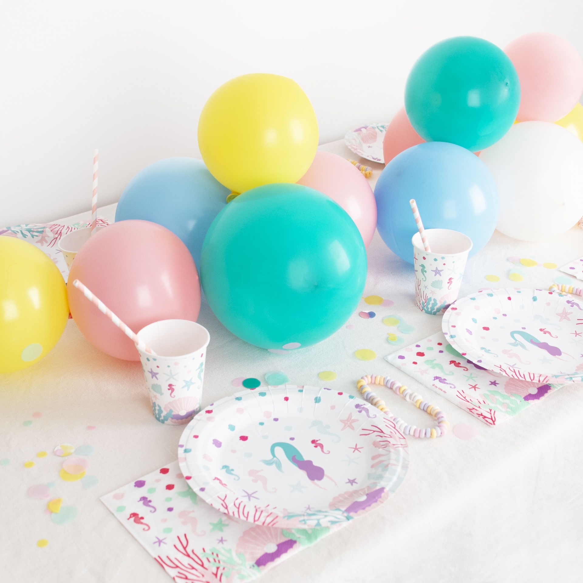 Decoração para festa infantil com balões coloridos e pratos de papel com desenhos de sereias