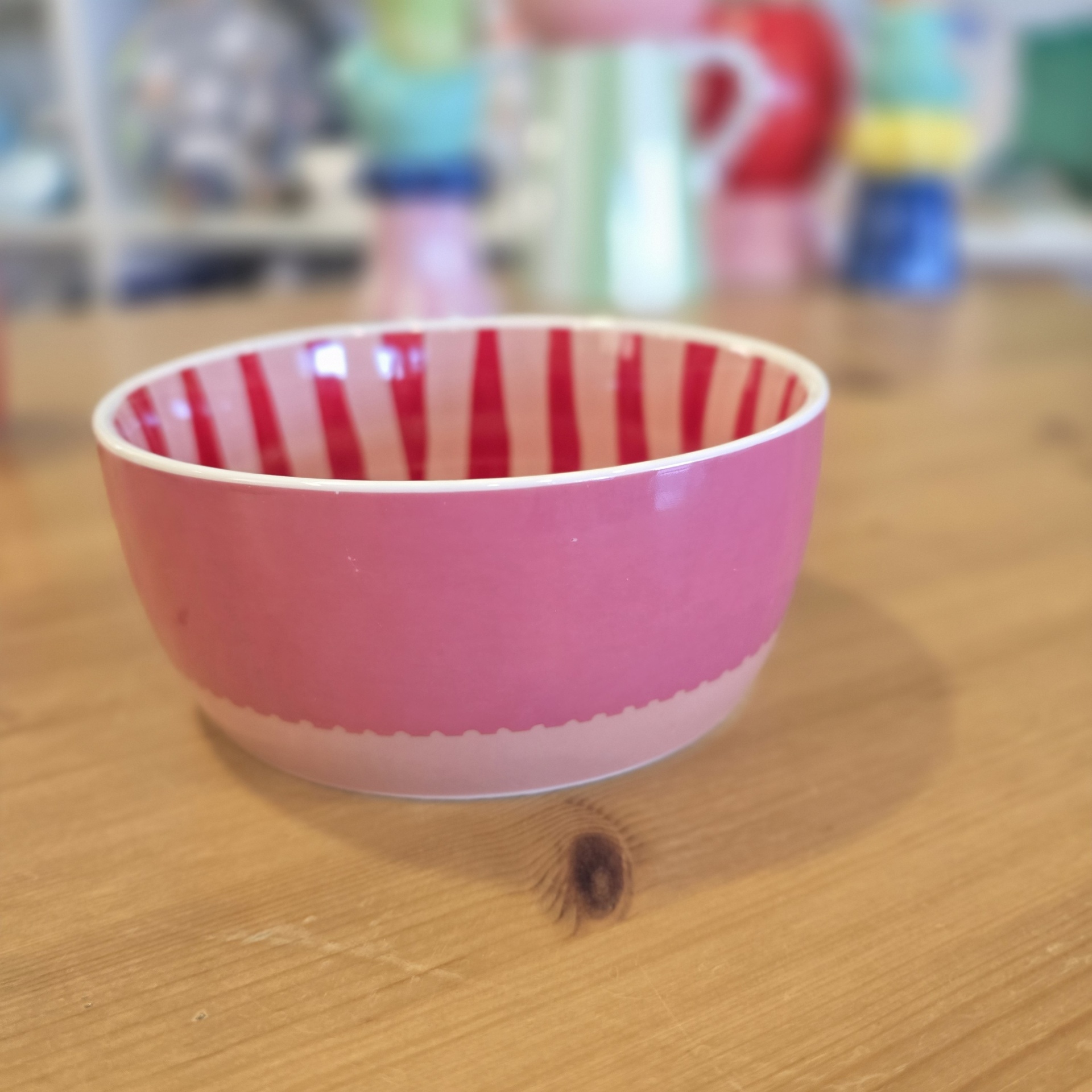 Taça cerâmica rosa com riscas vermelhas no interior, sobre mesa de madeira clara