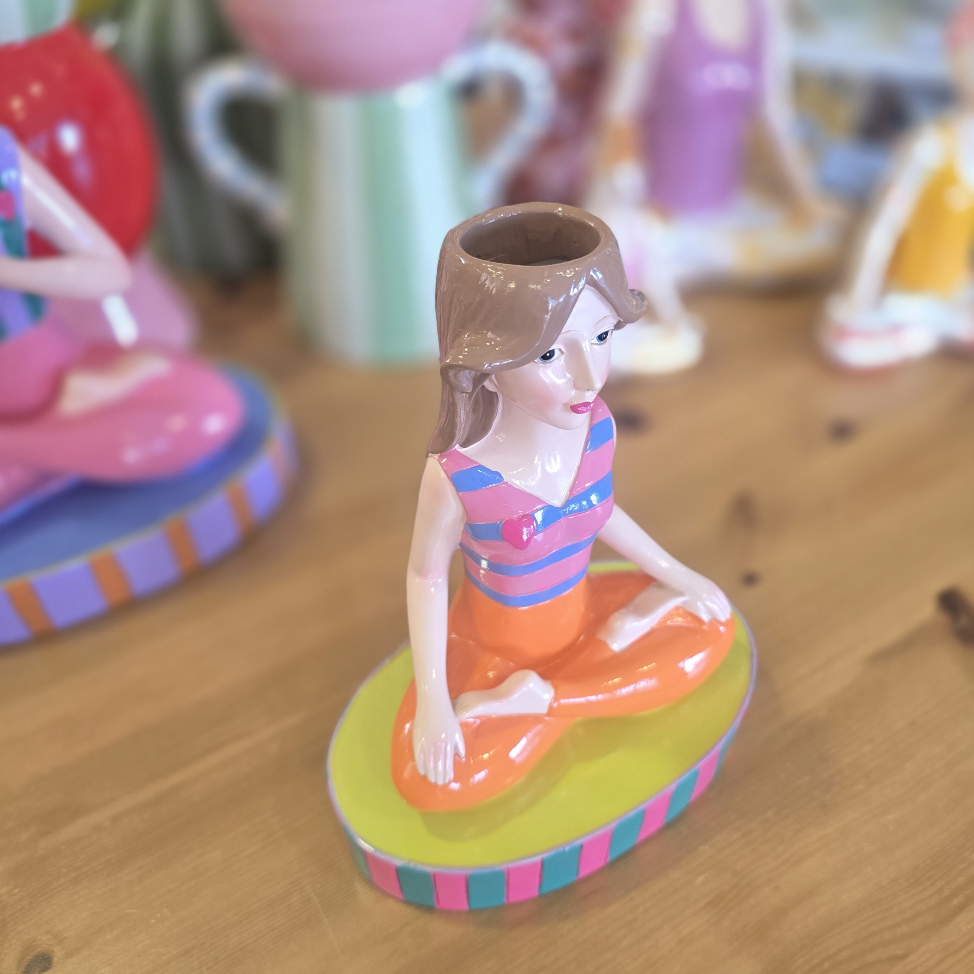 Escultura colorida de mulher a meditar sentada de pernas cruzadas com buraco na cabeça.