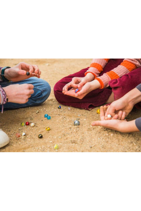 Crianças a jogar bolinhas coloridas no chão de terra