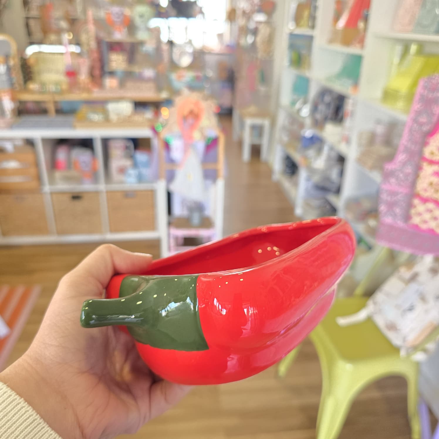 Taça cerâmica vermelha em forma de pimento com caule verde numa mão em loja