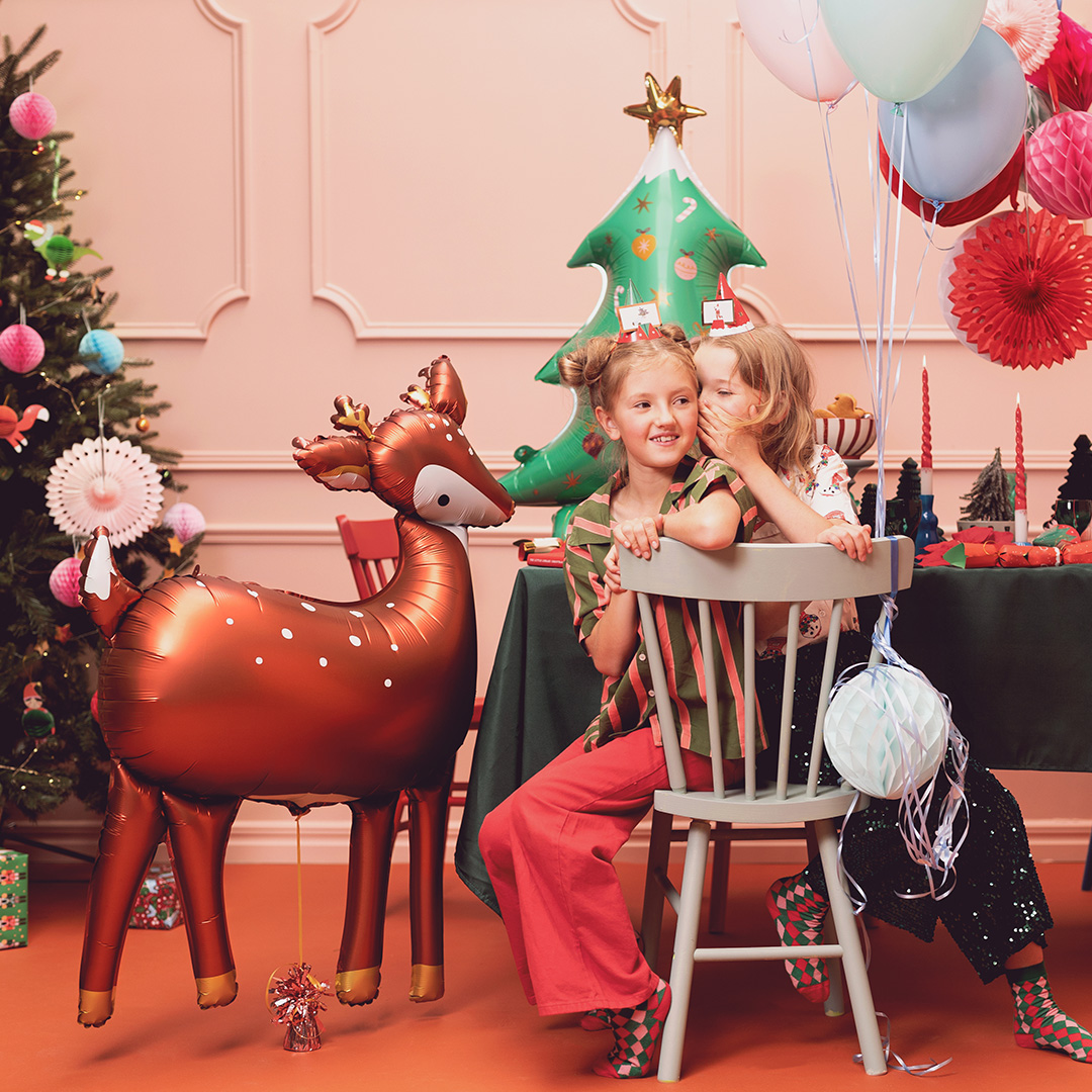 Crianças com balões e balão em forma de rena numa decoração natalícia