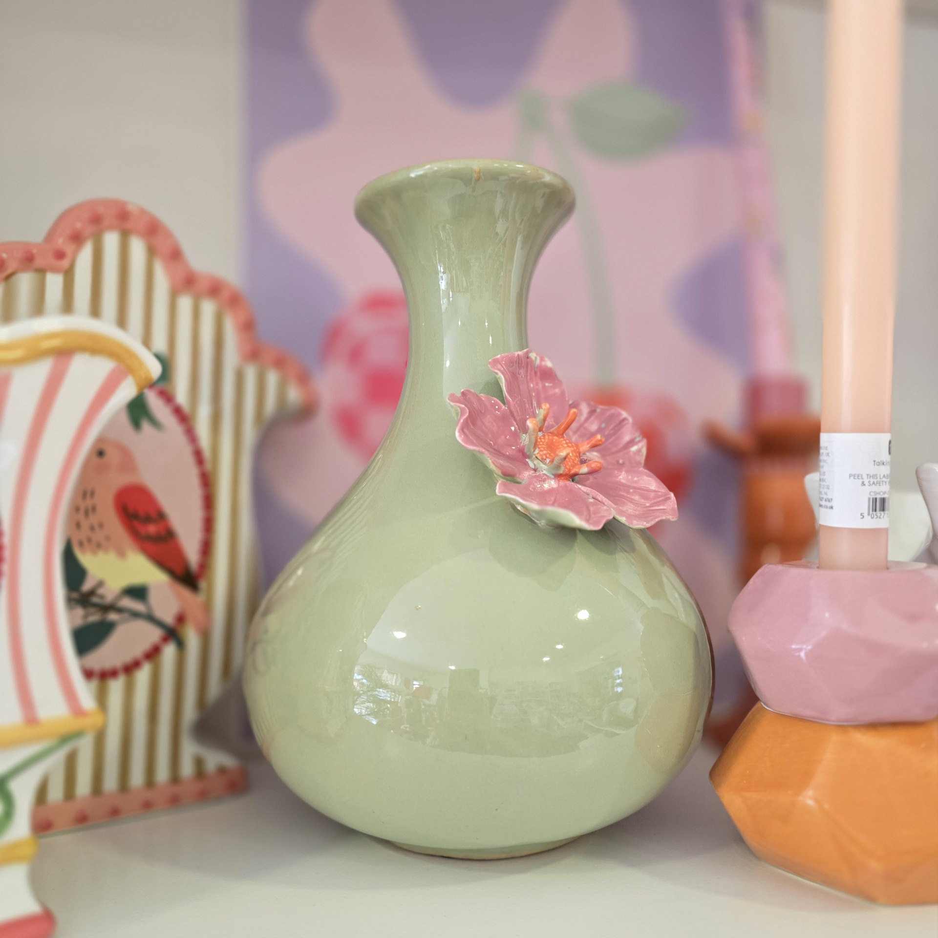 Vaso cerâmico verde com flor rosa e moldura decorativa ao fundo