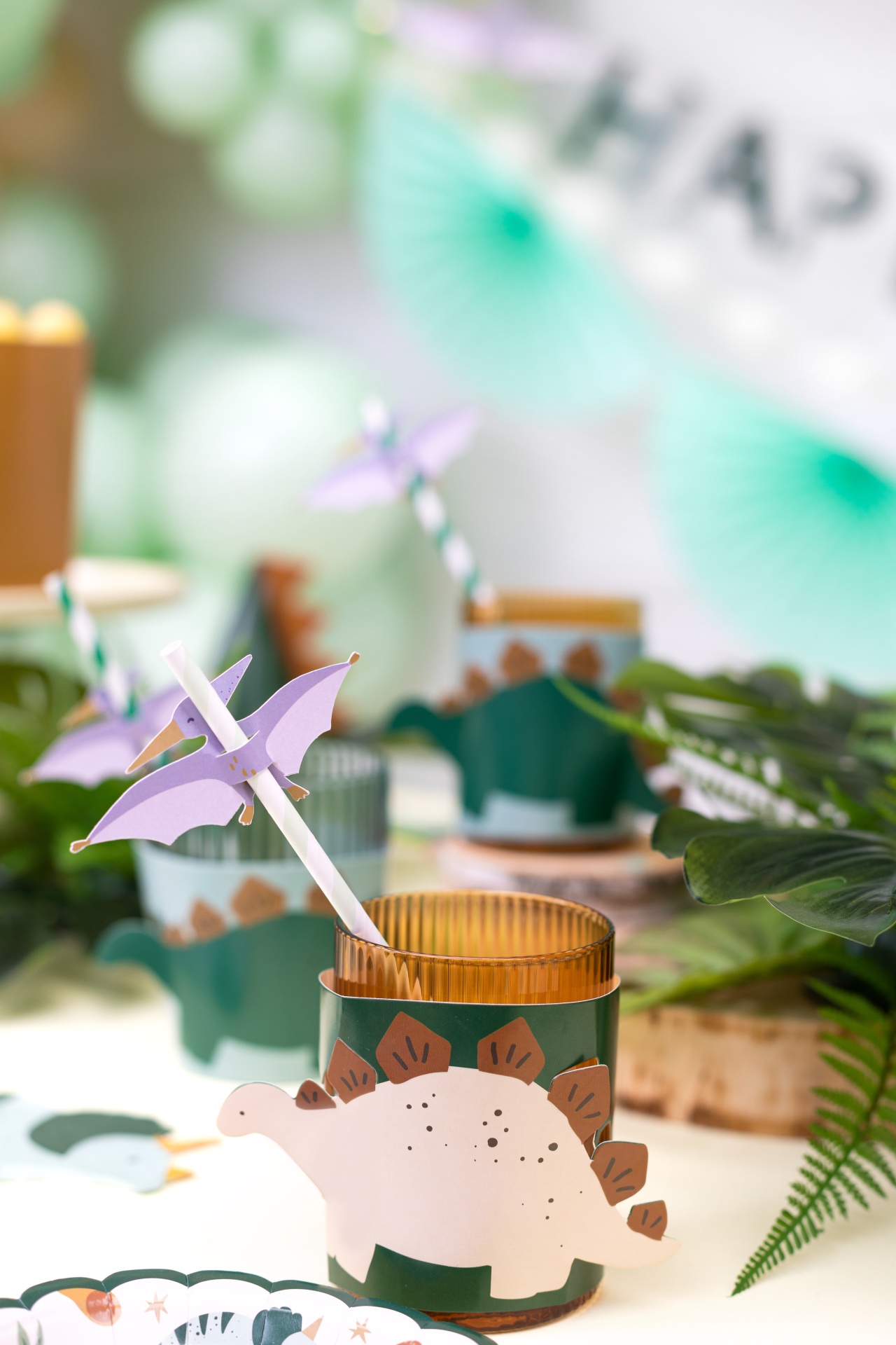 Copos de vidro com decoração de dinossauros e canudos com pterodátilos num ambiente decorado para festa