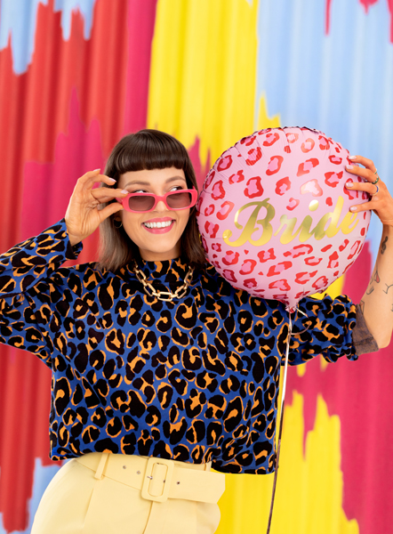 Mulher com blusa de leopardo segurando balão rosa 'Bride' com fundo colorido