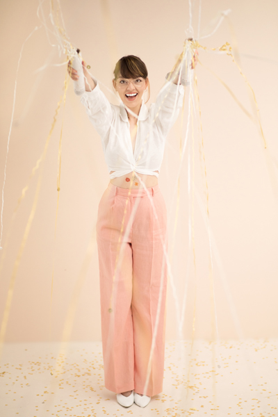 Mulher vestindo camisa branca e calças rosa segurando fitas douradas e brancas
