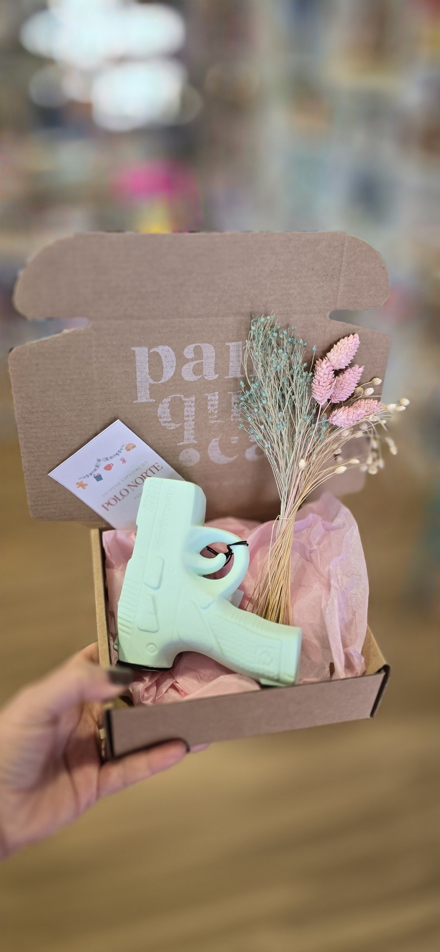 Caixa de cartão aberta com sabonete em forma de pistola e flores secas dentro