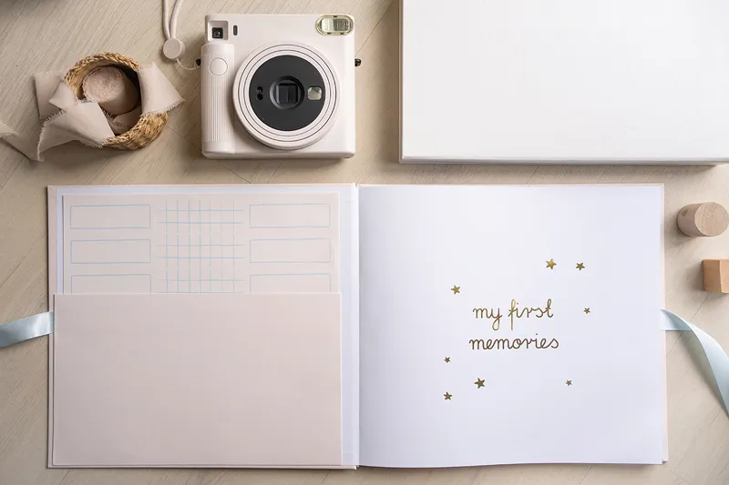 Álbum de fotos aberto com frase 'my first memories' e câmara fotográfica branca ao lado