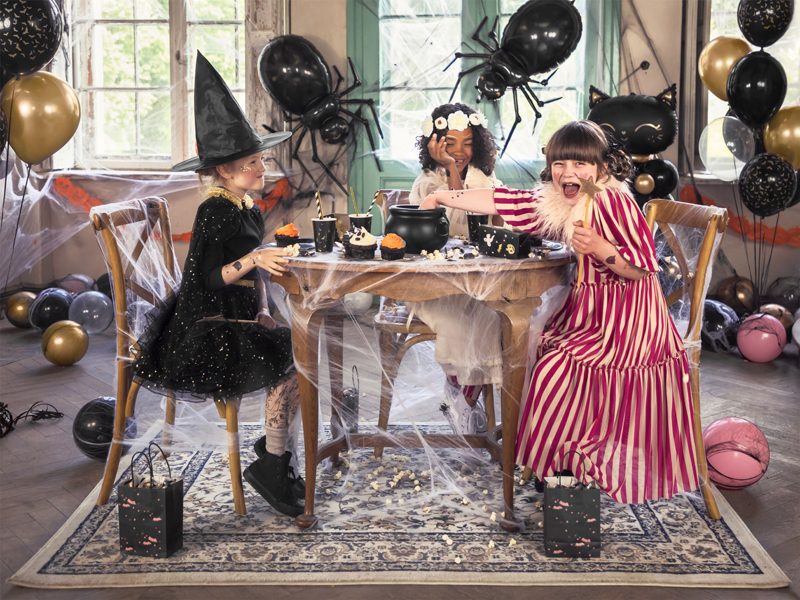 Crianças em fantasia de Halloween sentadas à mesa decorada com teias e balões