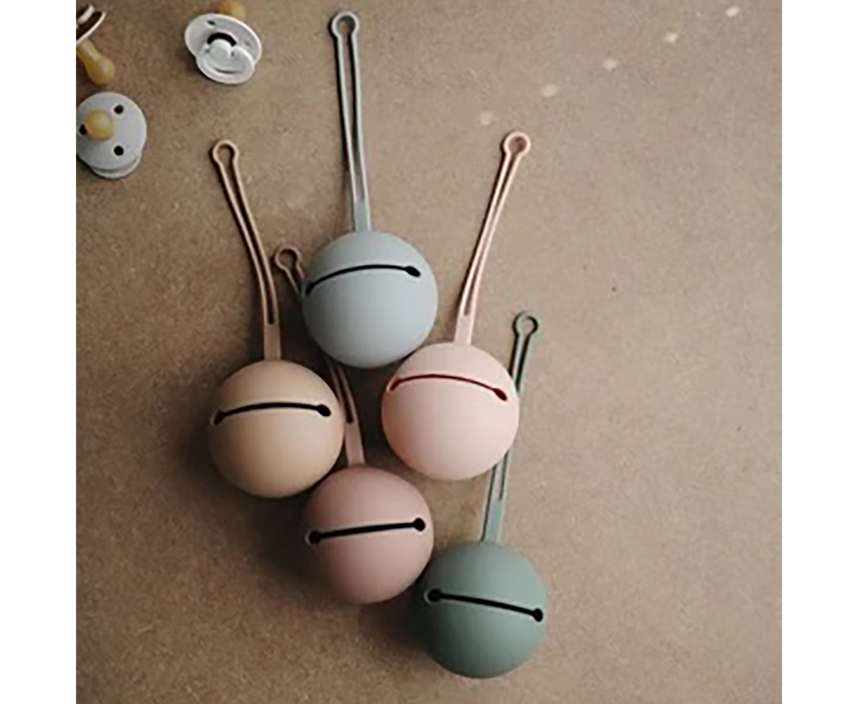 Cinco sinos de metal coloridos e chupetas sobre superfície bege