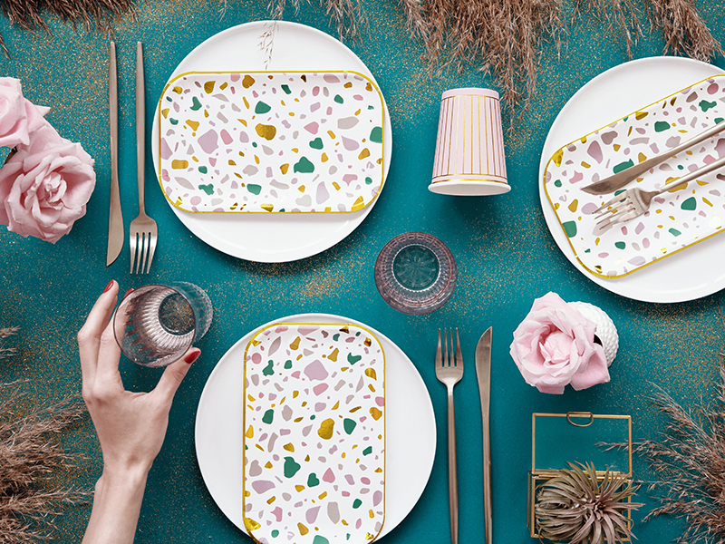 Conjunto de loiça e talheres com padrão terrazzo sobre mesa azul