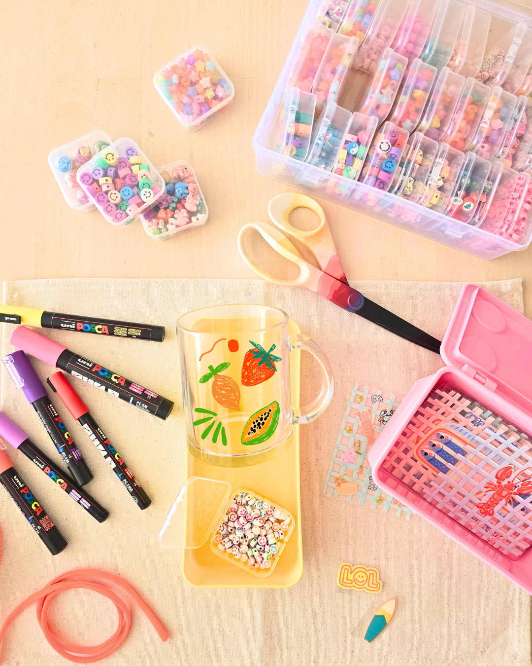 Material criativo com canetas, contas coloridas e caneca de vidro com desenhos de frutas