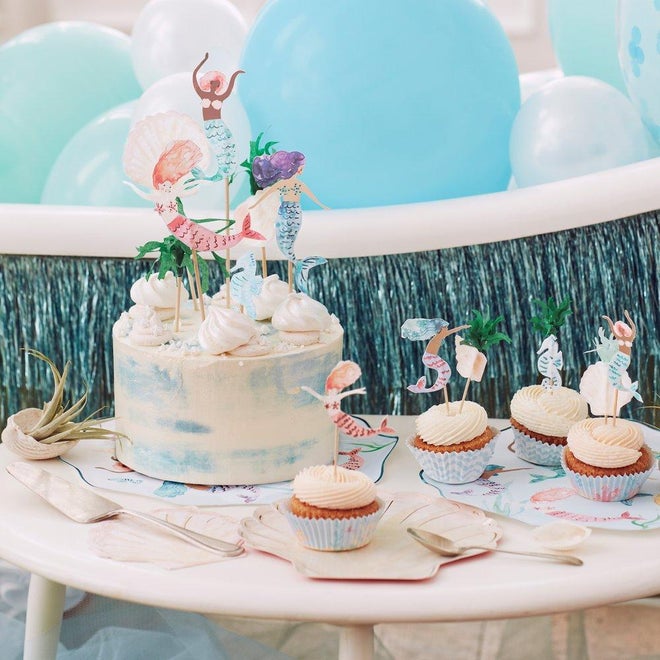 Bolo e cupcakes decorados com tema de sereias sobre mesa branca