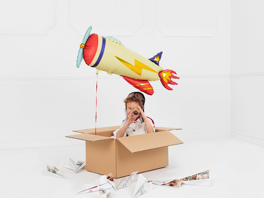 Balão foguete amarelo e criança em caixa de cartão com aviões de papel