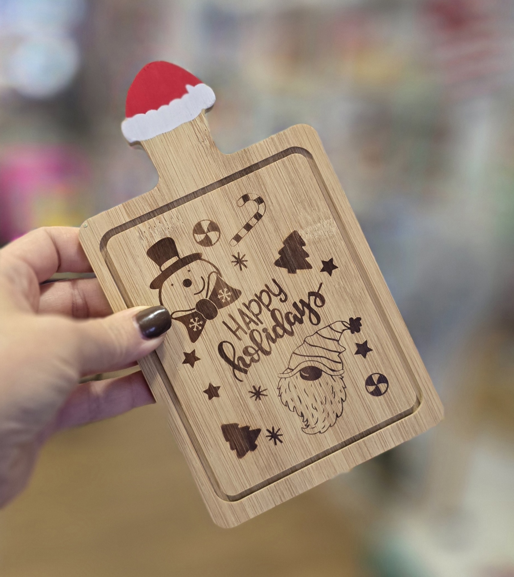 Tábua de corte de madeira com decoração natalícia e texto 'HAPPY holidays', com chapéu de Natal na pega