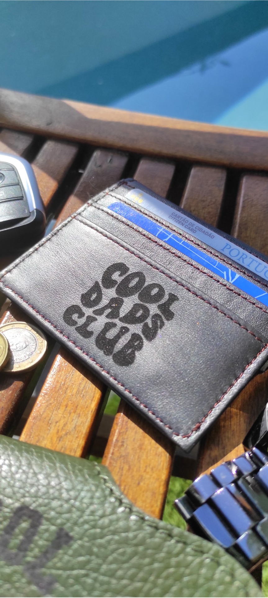 Carteira castanha escura de pele com texto COOL DADS CLUB sobre banco de madeira