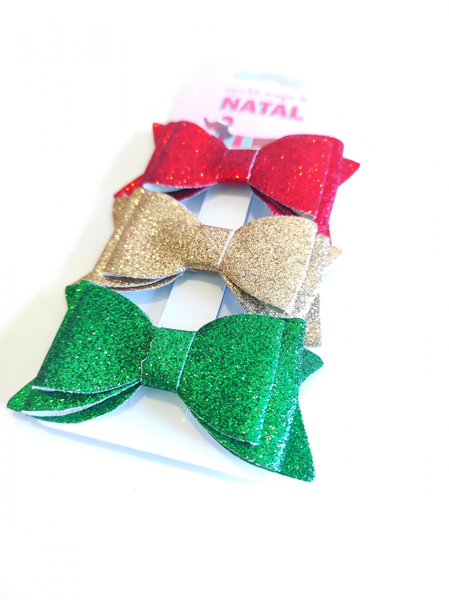 Três laços com glitter vermelhos, dourados e verdes para decoração de Natal num cartão branco