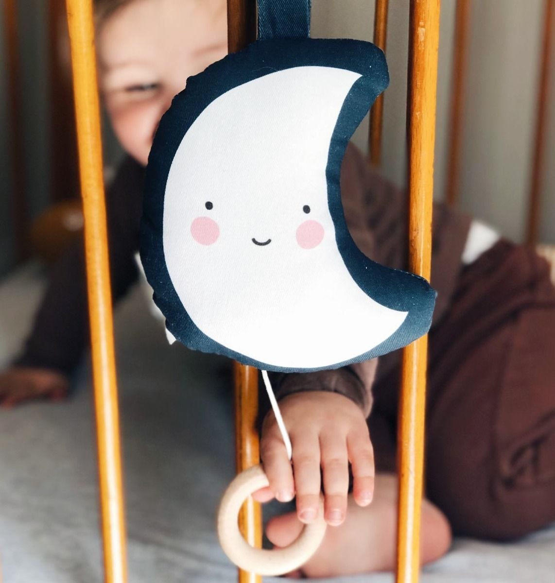 Brinquedo de lua sorridente em tecido com criança ao fundo