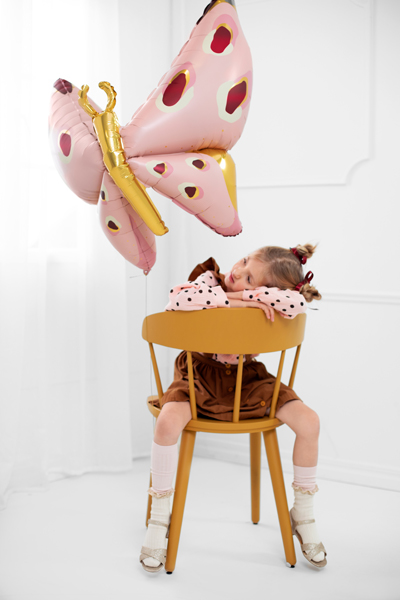 Balão foil borboleta cor-de-rosa junto a criança numa cadeira amarela