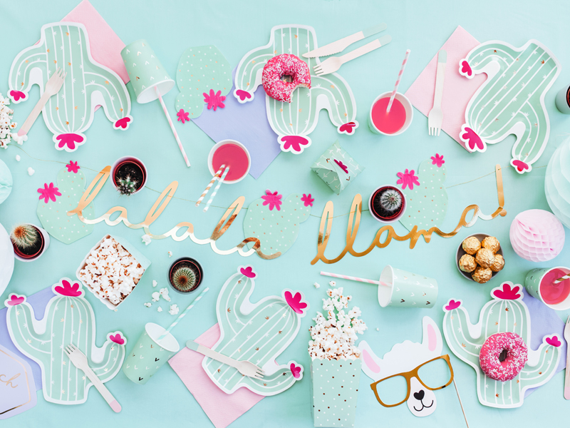 Mesa de festa com decoração de cactos, donuts cor-de-rosa, pipocas, letras douradas e desenho de llama usando óculos.