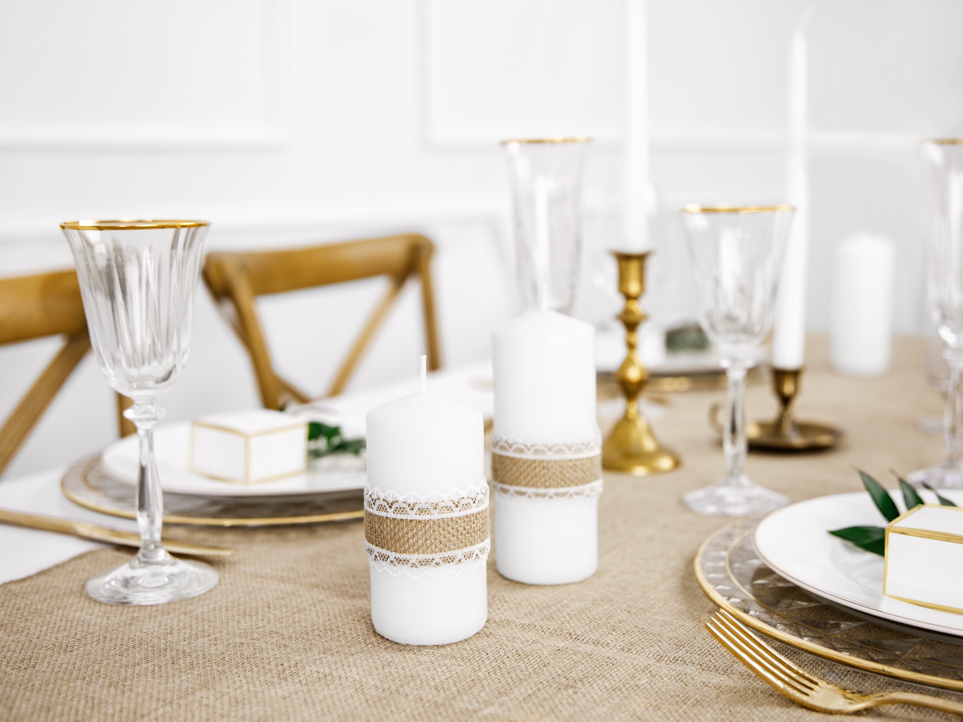 Mesa posta com velas brancas, castiçais dourados e copos de vidro com detalhes dourados