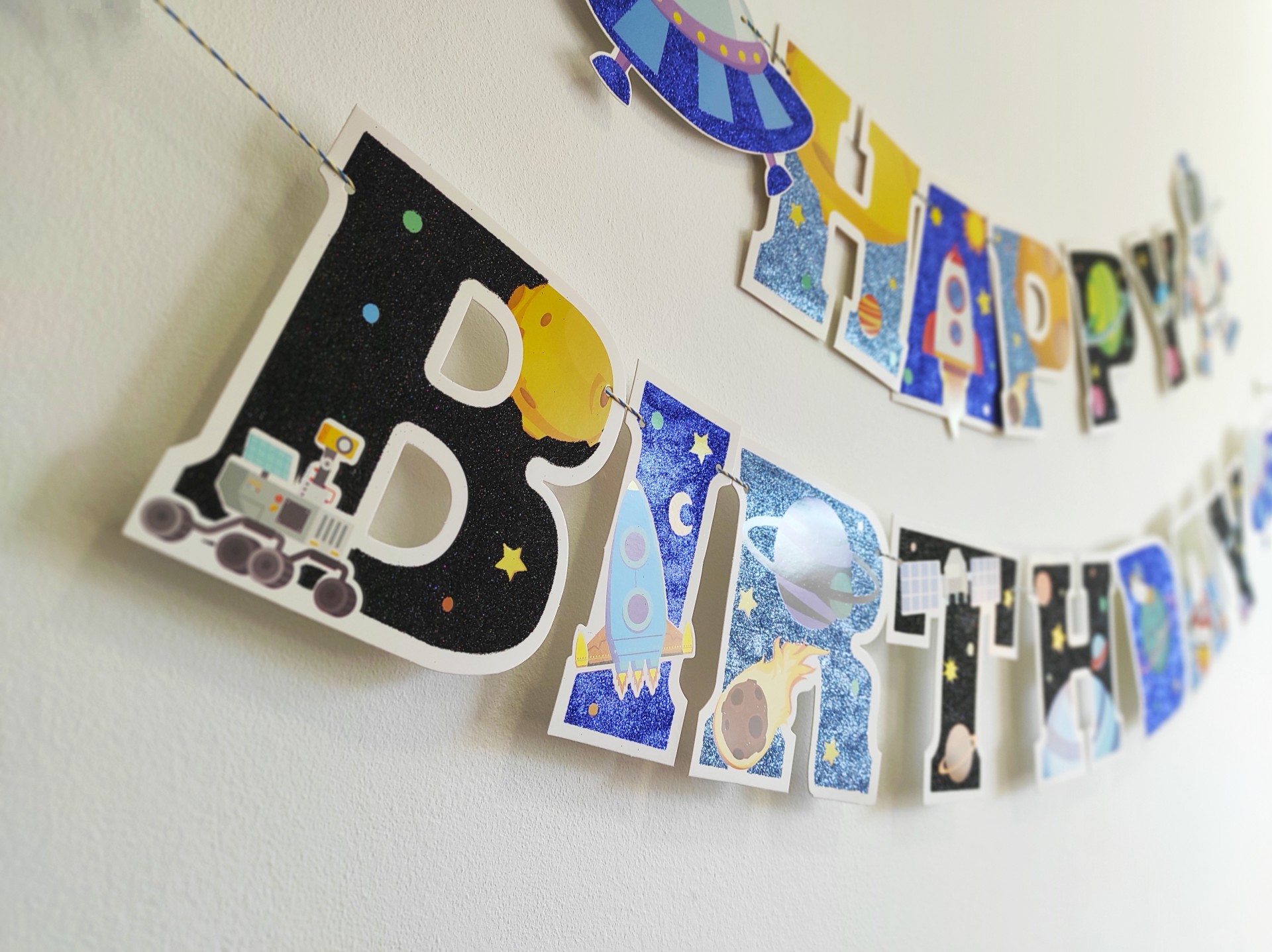 Guirlanda de papel com tema espacial e letras coloridas para aniversário pendurada na parede