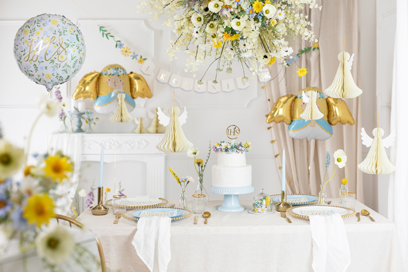 Mesa de festa decorada com bolo branco, balões com anjos dourados e azuis, e balão redondo com texto it’s a boy.
