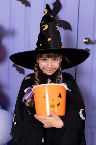Menina com fantasia de bruxa e balde de abóbora sorridente