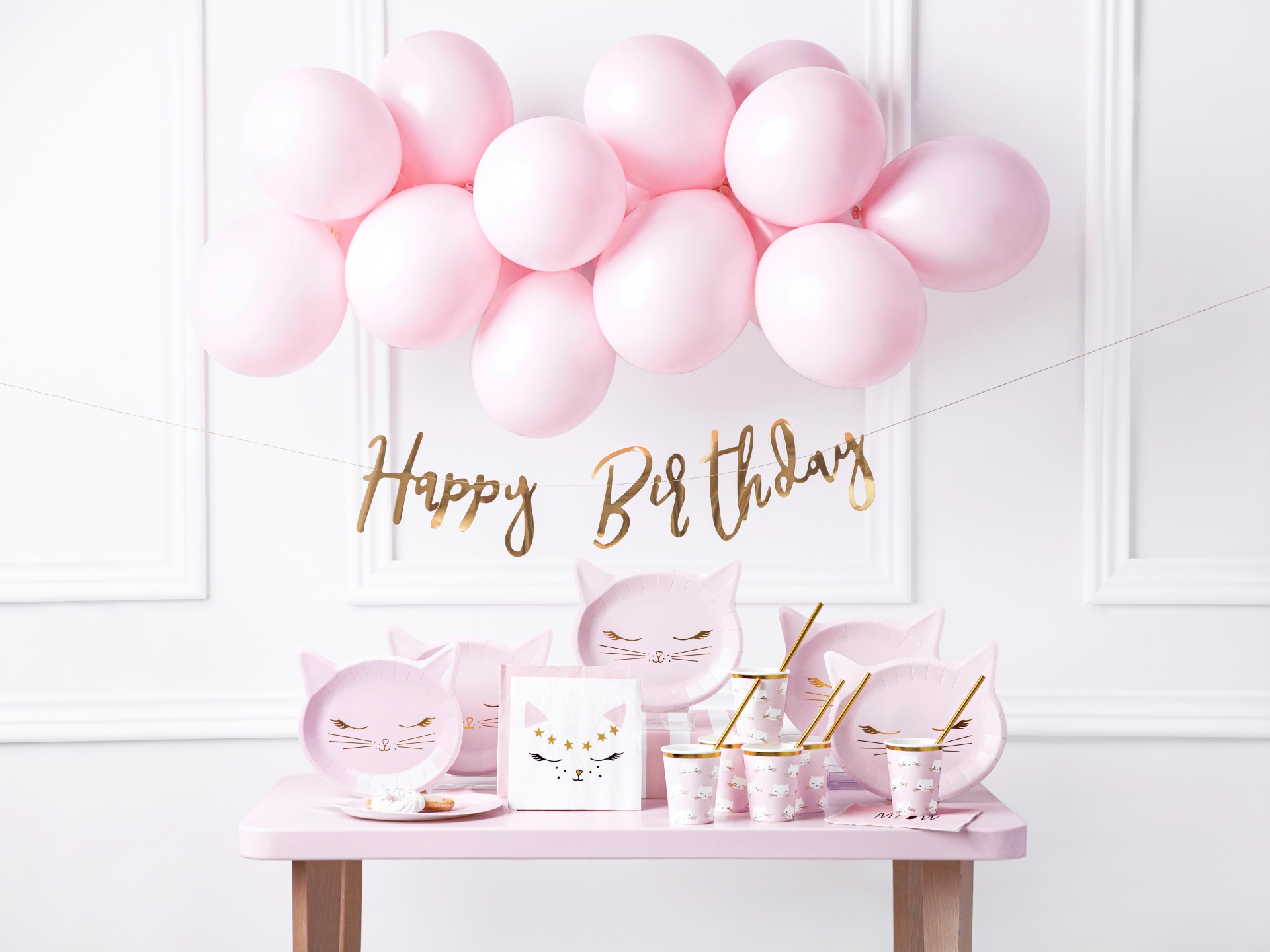 Decoração de festa com balões cor-de-rosa, texto 'Happy Birthday' e utensílios com desenho de gato cor-de-rosa.