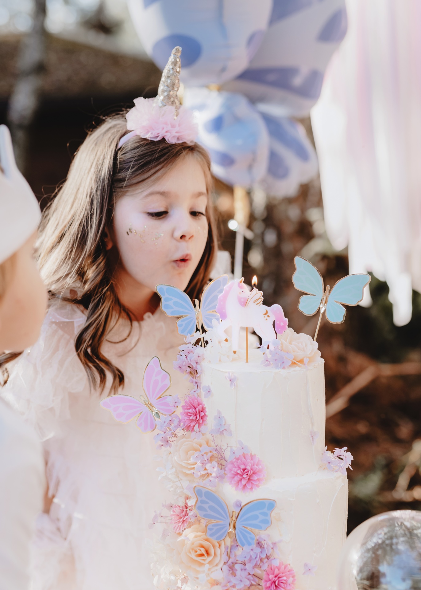 Bolo de aniversário branco com flores e borboletas decorativas e vela de unicórnio
