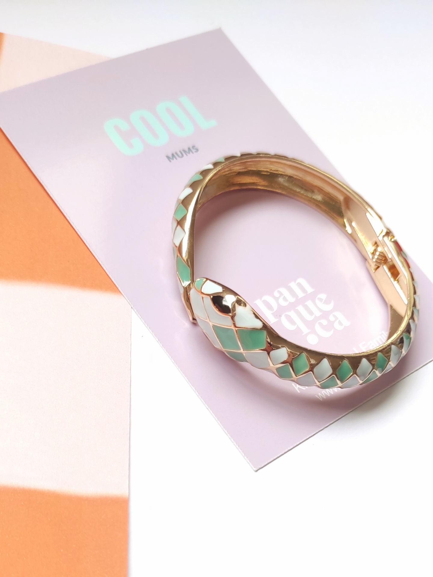 Pulseira dourada com padrão verde e branco em cartão lilás com texto