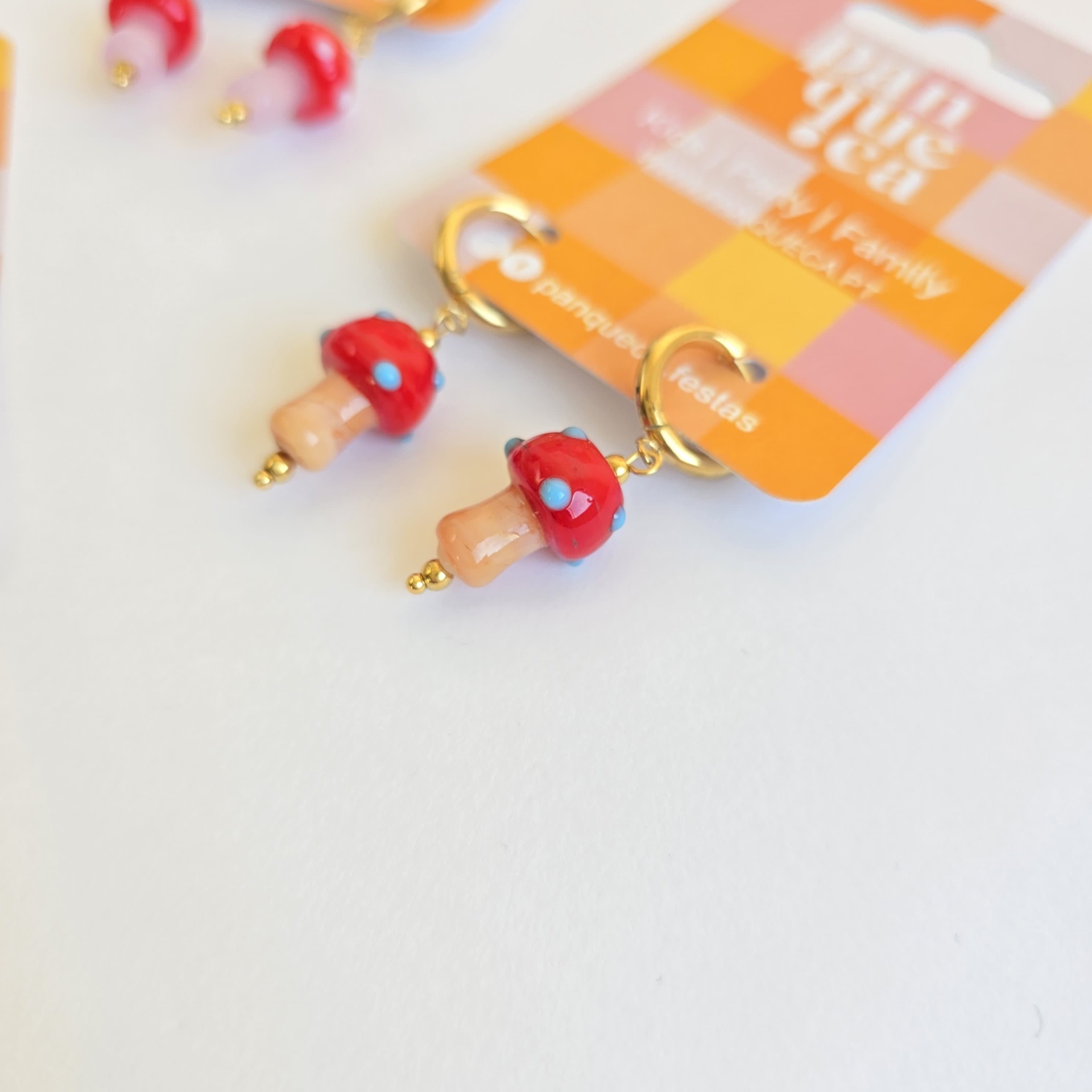 Brincos em forma de cogumelo com chapéu vermelho e bolinhas azuis num cartão colorido