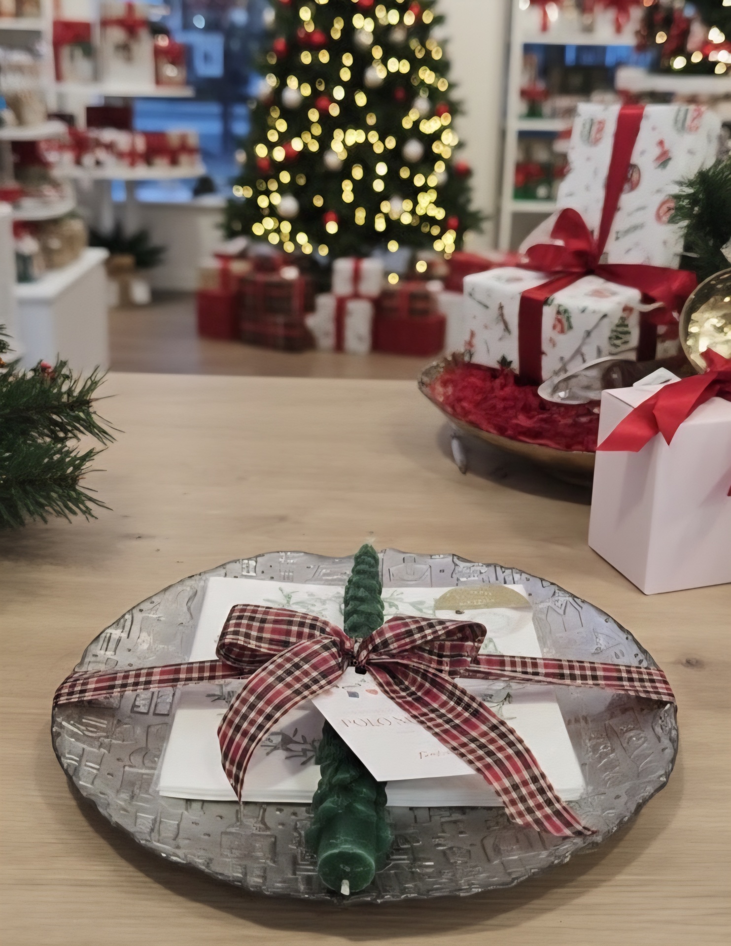 Prato decorativo com vela, guardanapo e fita xadrez em mesa de madeira com decoração natalícia ao fundo