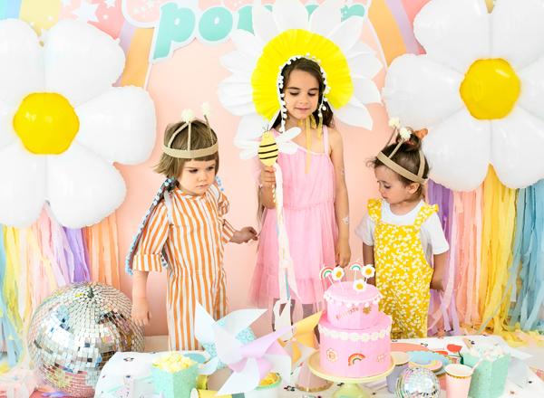 Crianças em festa com bolo rosa e decoração floral colorida