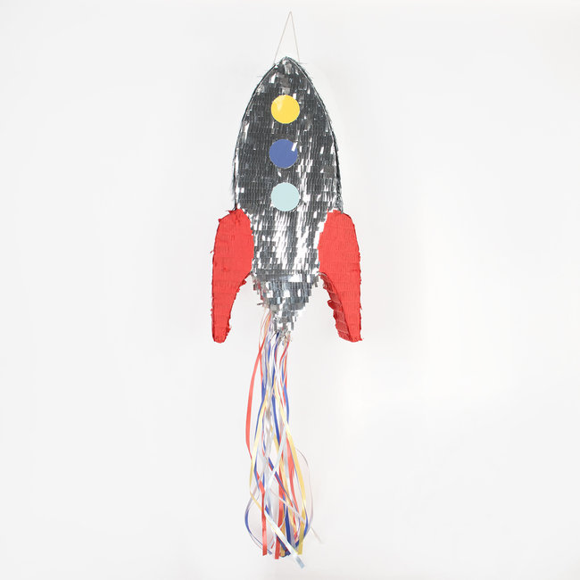Piñata em forma de foguete prateado com asas vermelhas e fitas coloridas penduradas.