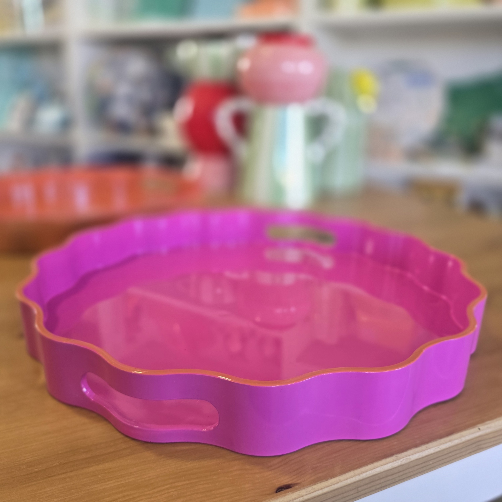 Tabuleiro de serviço rosa com borda ondulada e pega, sobre superfície de madeira