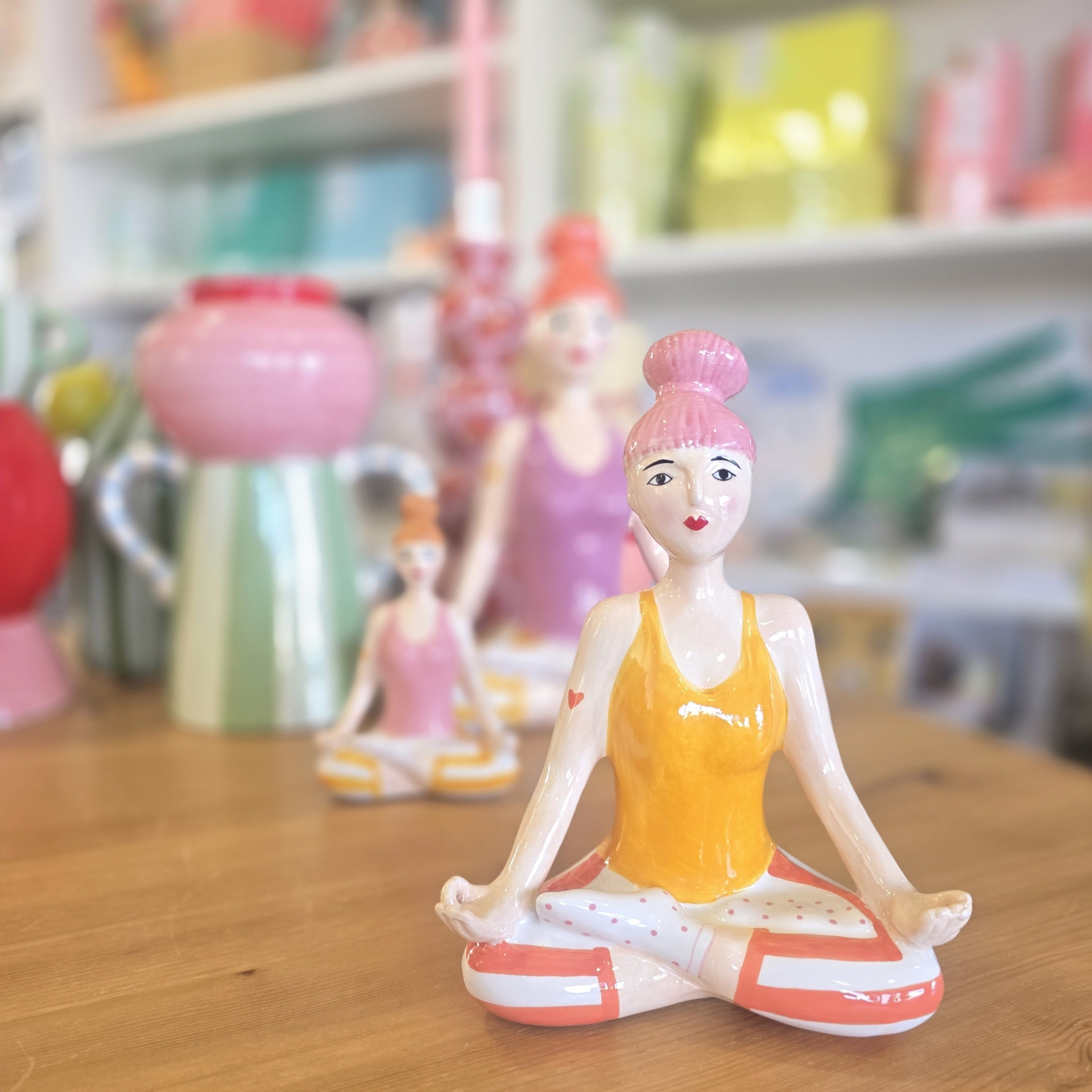 Figuras cerâmicas femininas em pose de ioga com roupas coloridas sobre mesa de madeira