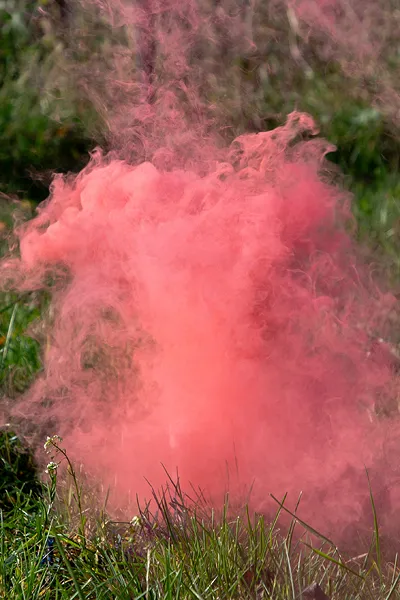 Nuvem densa de fumo cor-de-rosa saindo do chão com relva verde