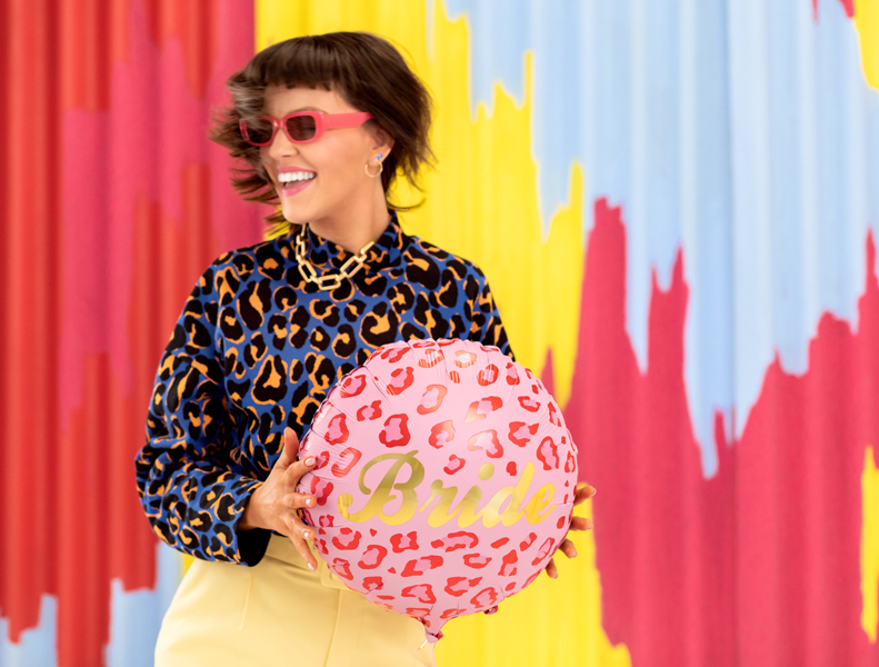 Mulher com blusa animal print e saia amarela segurando bola rosa com texto Bride