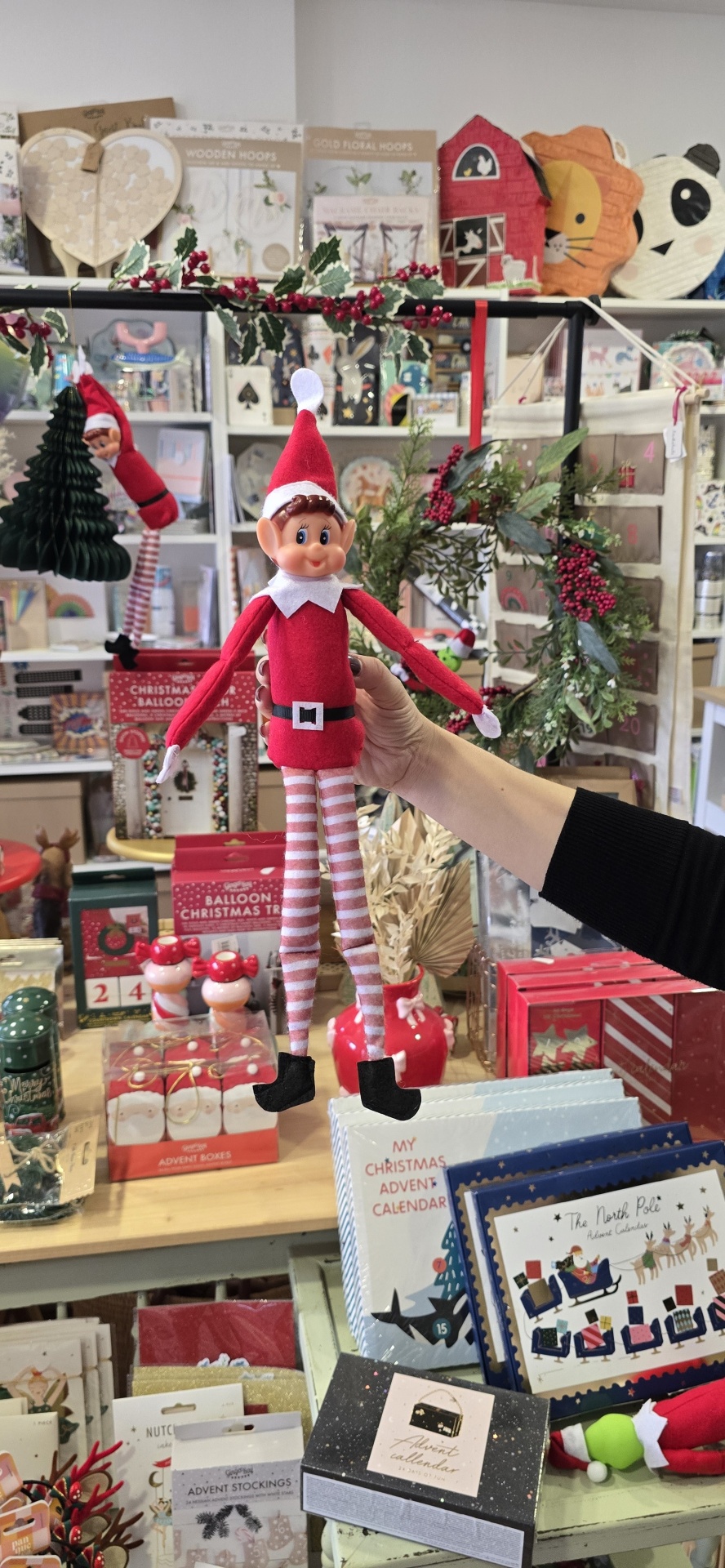 Boneco elfo de Natal com roupa vermelha e calças às riscas num ambiente decorativo de Natal