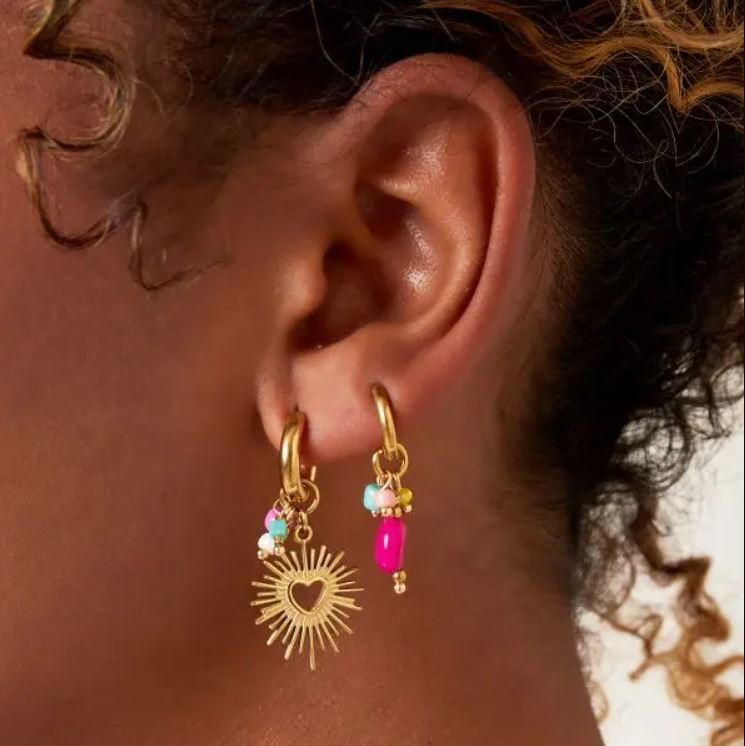 Brincos dourados com pendentes coloridos numa orelha de pele escura
