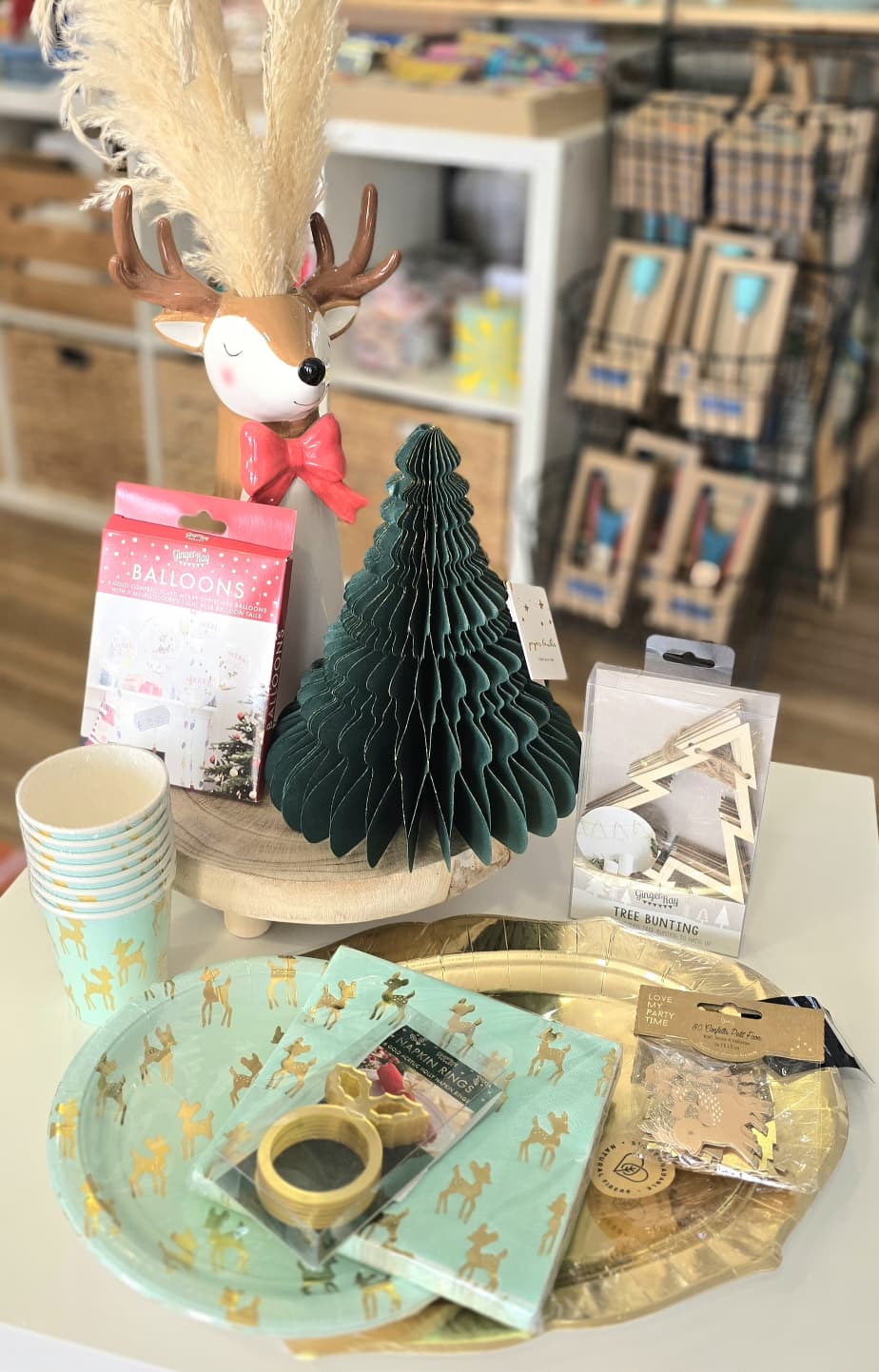 Artigos festivos de Natal em mesa com árvore de papel, pratos, copos e decoração de rena