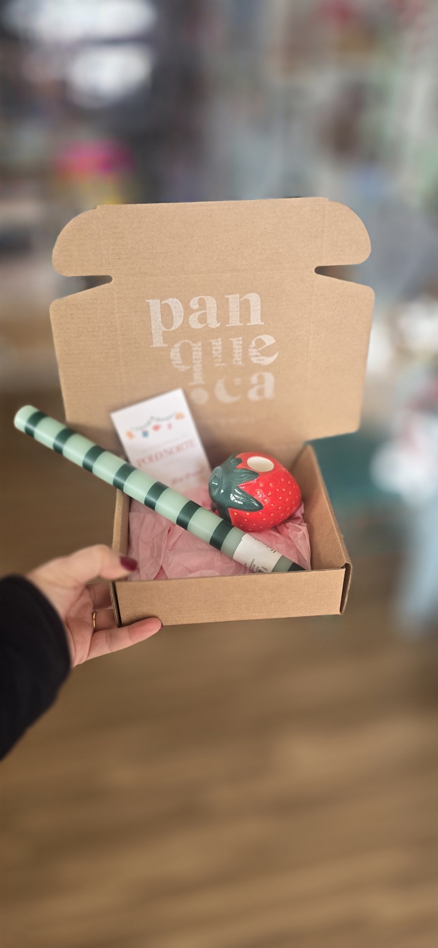 Caixa de cartão castanho aberta com itens dentro, incluindo uma mangueira riscada e um objecto vermelho semelhante a morango