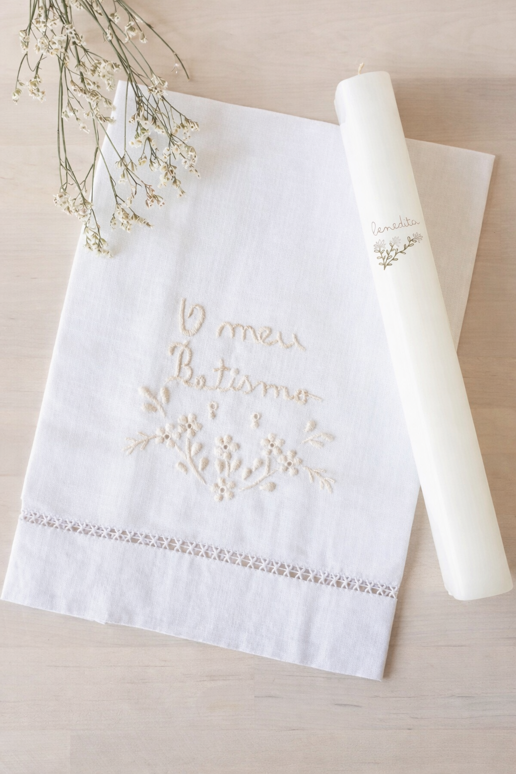 Guardanapo de linho branco com bordado O meu Batismo e vela branca com rf3tulo benedita, junto de flores secas sobre fundo claro